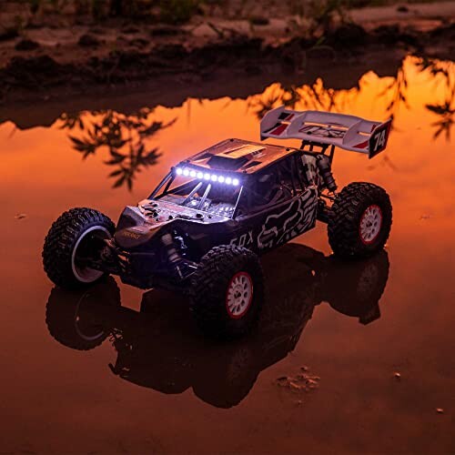 Remote control car with lights on, reflected in water at sunset.